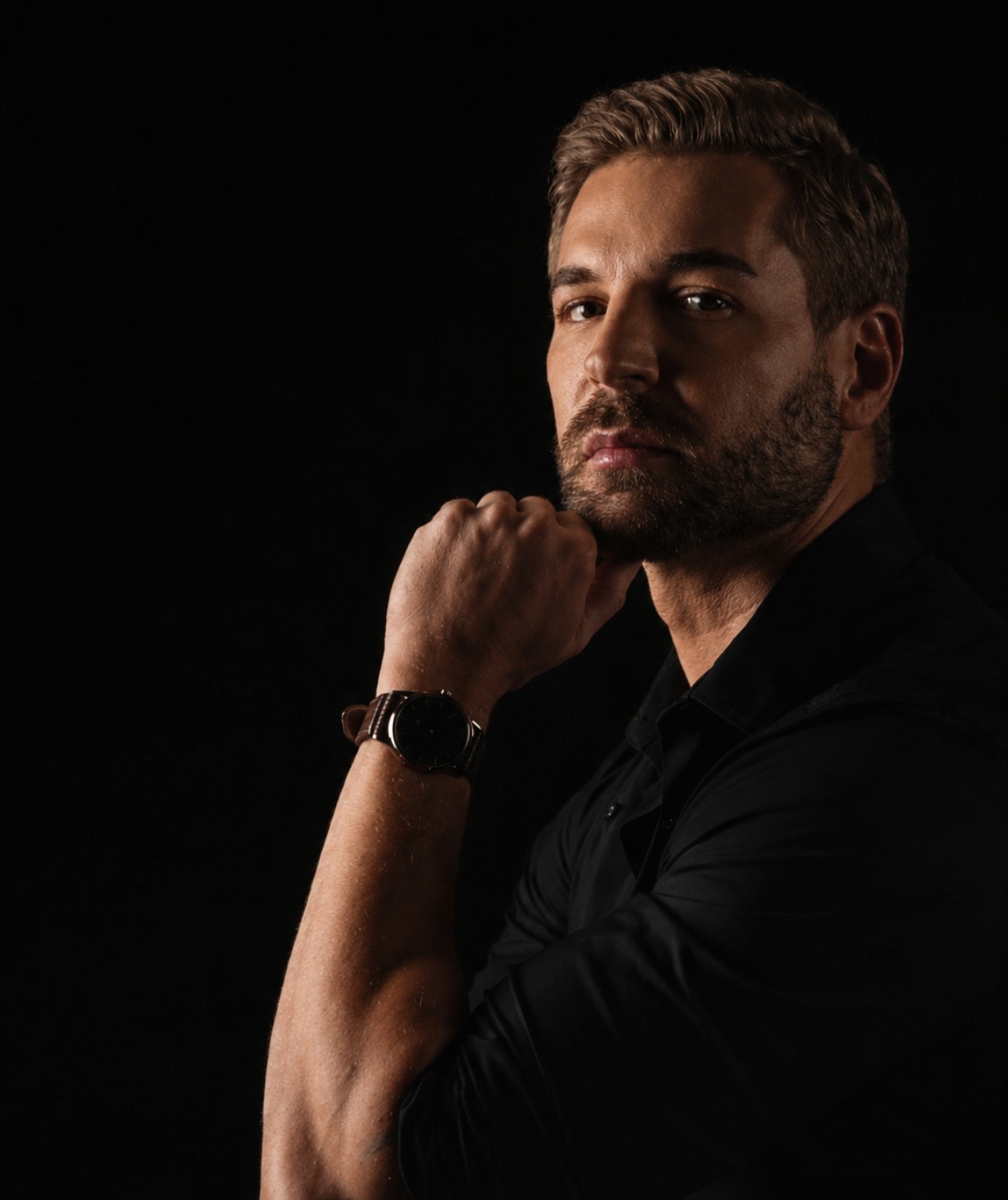 Justin Duwe photographed against a black background, hand resting at his chin